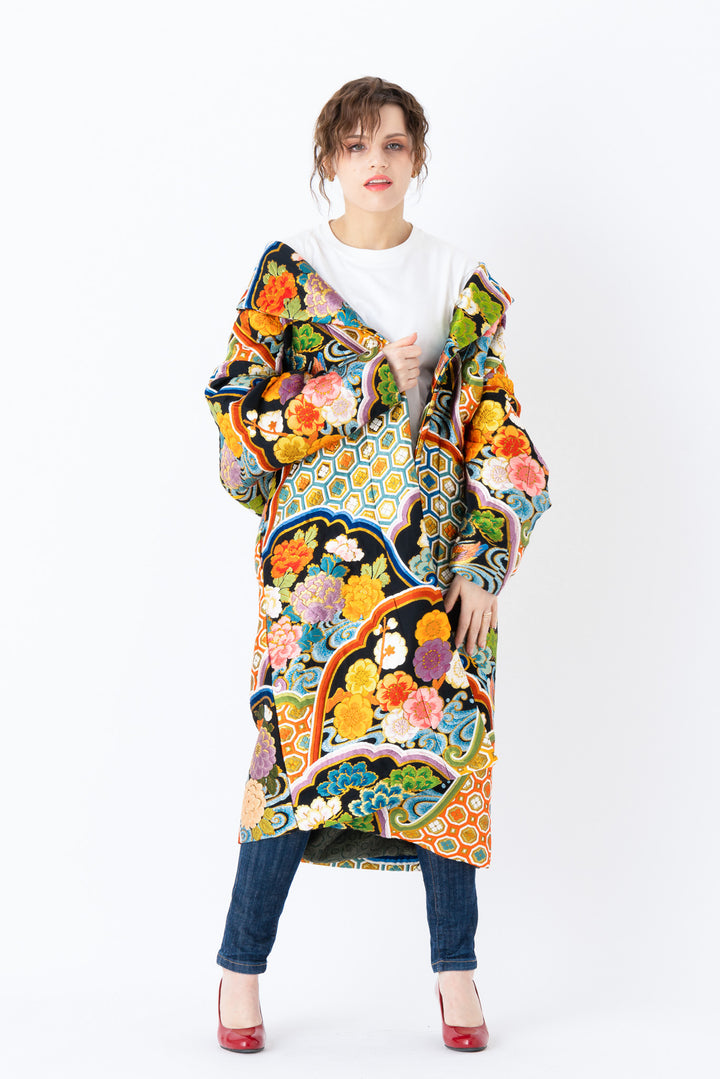 A woman is wearing an oversized silk coat for women. This long silk coat embodies the essence of a long coat for women. Its surface is adorned with intricate silk embroidery, exemplifying the artistry behind a silk embroidered coat for women. The coat's length accentuates its elegance, making it a perfect representation of a long embroidered coat. The oversized nature of this oversized coat for women adds a touch of grandeur to the ensemble, combining style and comfort seamlessly.
