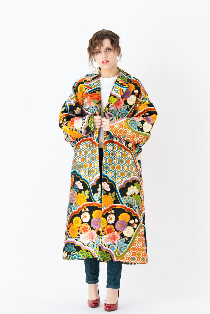A woman is wearing an oversized silk coat for women. This long silk coat embodies the essence of a long coat for women. Its surface is adorned with intricate silk embroidery, exemplifying the artistry behind a silk embroidered coat for women. The coat's length accentuates its elegance, making it a perfect representation of a long embroidered coat. The oversized nature of this oversized coat for women adds a touch of grandeur to the ensemble, combining style and comfort seamlessly.