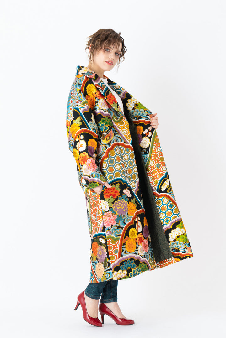 A woman is wearing an oversized silk coat for women. This long silk coat embodies the essence of a long coat for women. Its surface is adorned with intricate silk embroidery, exemplifying the artistry behind a silk embroidered coat for women. The coat's length accentuates its elegance, making it a perfect representation of a long embroidered coat. The oversized nature of this oversized coat for women adds a touch of grandeur to the ensemble, combining style and comfort seamlessly.