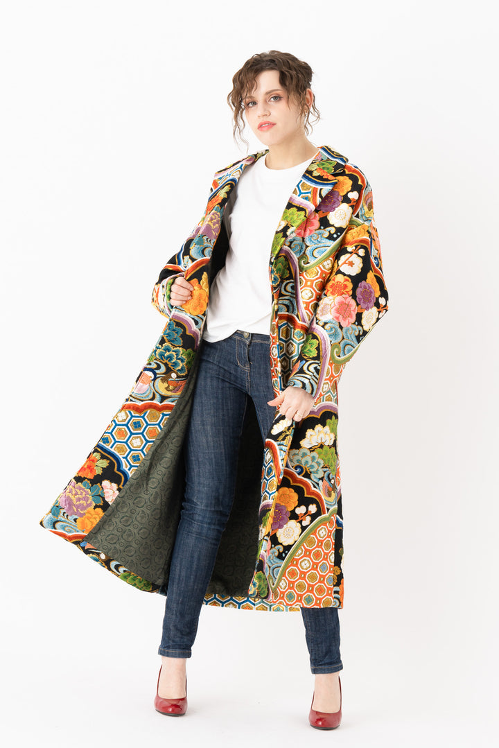 A woman is wearing an oversized silk coat for women. This long silk coat embodies the essence of a long coat for women. Its surface is adorned with intricate silk embroidery, exemplifying the artistry behind a silk embroidered coat for women. The coat's length accentuates its elegance, making it a perfect representation of a long embroidered coat. The oversized nature of this oversized coat for women adds a touch of grandeur to the ensemble, combining style and comfort seamlessly.