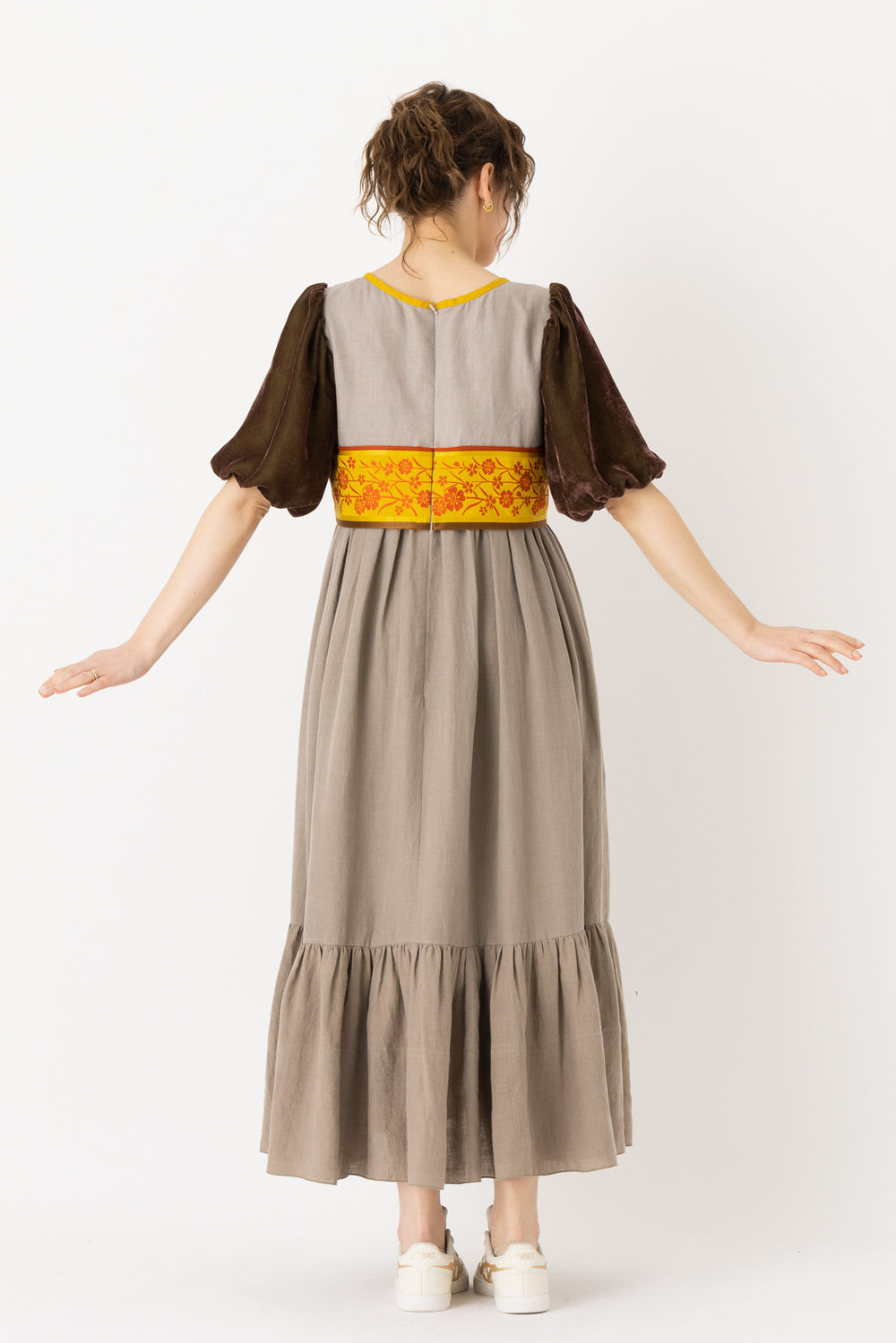 A woman is wearing an empire dress with a classic empire waist, showcasing an empire style dress. This empire waist dress is quite long, making it an example of a high waist maxi dress. This high waist dress enhances her figure. This maxi empire dress exudes sophistication and elegance making it ideal for a formal occasion or a leisurely evening out.