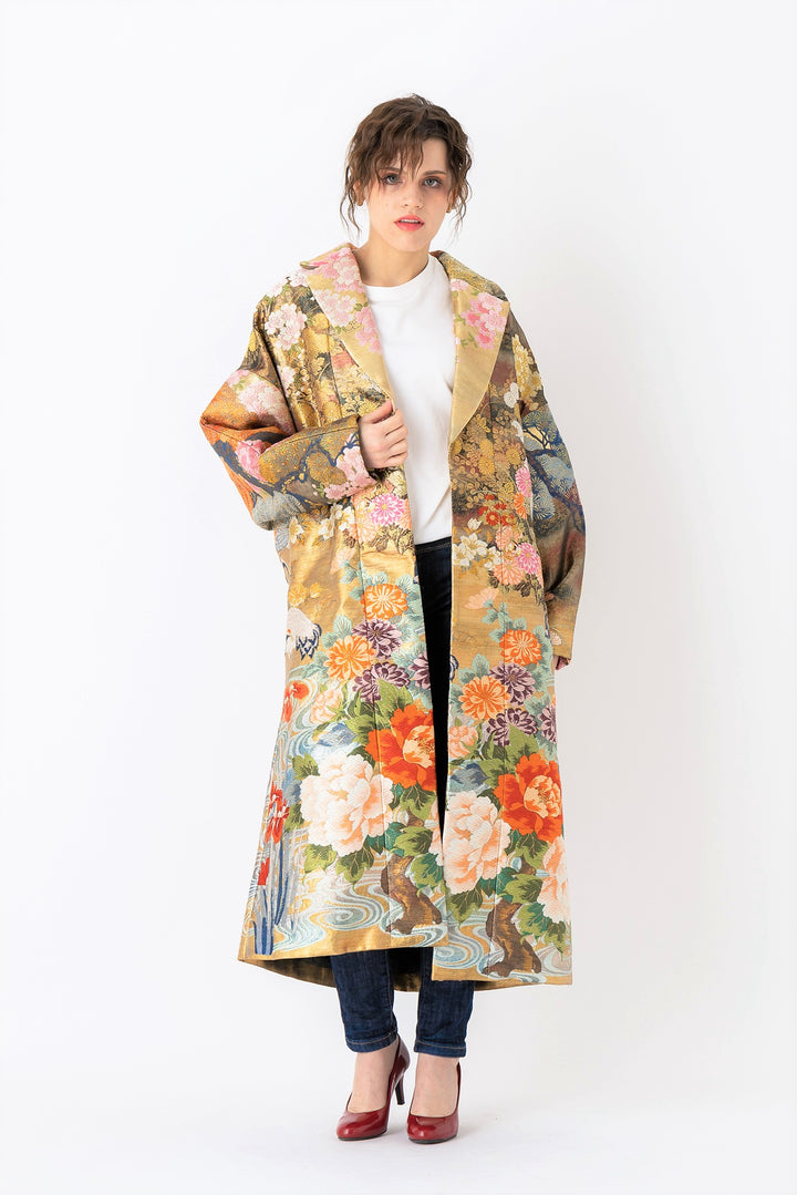 A woman is wearing an oversized silk coat for women. This long silk coat embodies the essence of a long coat for women. Its surface is adorned with intricate silk embroidery, exemplifying the artistry behind a silk embroidered coat for women. The coat's length accentuates its elegance, making it a perfect representation of a long embroidered coat. The oversized nature of this oversized coat for women adds a touch of grandeur to the ensemble, combining style and comfort seamlessly.