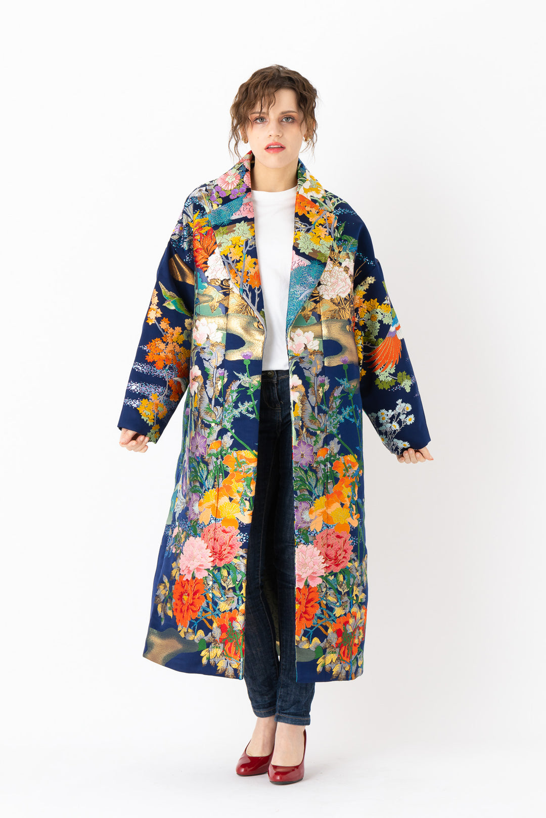 A woman is wearing an oversized silk coat for women. This long silk coat embodies the essence of a long coat for women. Its surface is adorned with intricate silk embroidery, exemplifying the artistry behind a silk embroidered coat for women. The coat's length accentuates its elegance, making it a perfect representation of a long embroidered coat. The oversized nature of this oversized coat for women adds a touch of grandeur to the ensemble, combining style and comfort seamlessly. 