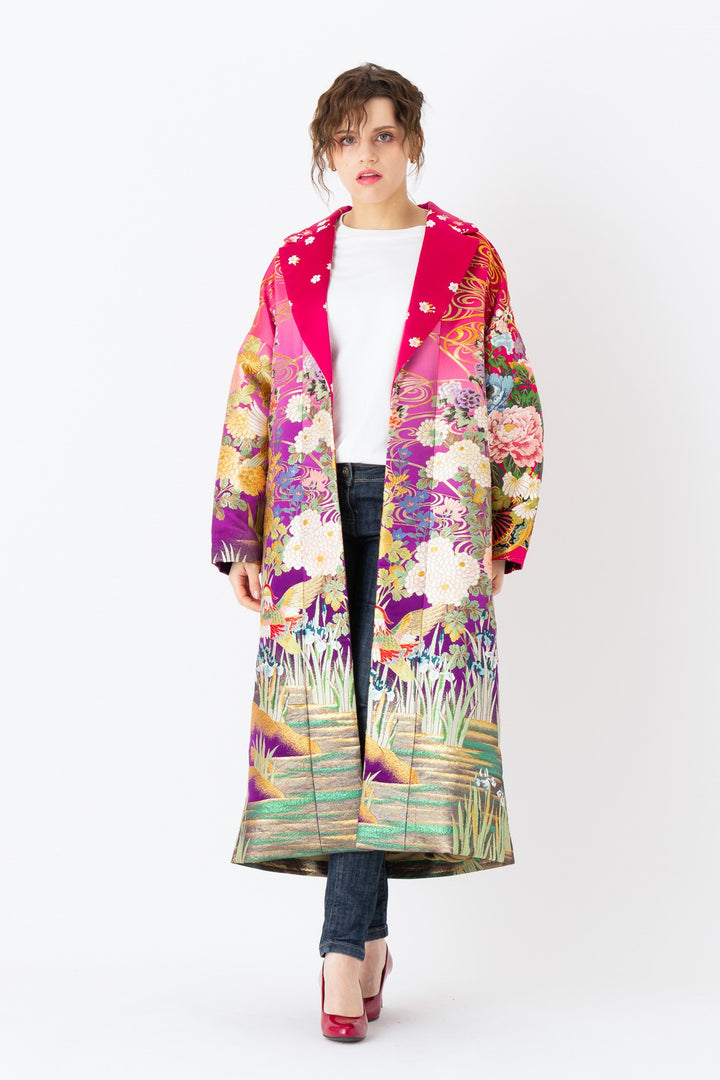 A woman is wearing an oversized silk coat for women. This long silk coat embodies the essence of a long coat for women. Its surface is adorned with intricate silk embroidery, exemplifying the artistry behind a silk embroidered coat for women. The coat's length accentuates its elegance, making it a perfect representation of a long embroidered coat. The oversized nature of this oversized coat for women adds a touch of grandeur to the ensemble, combining style and comfort seamlessly. 