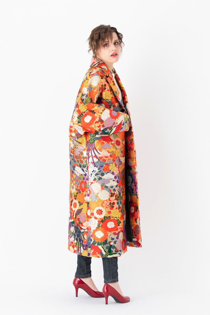 A woman is wearing an oversized silk coat for women. This long silk coat embodies the essence of a long coat for women. Its surface is adorned with intricate silk embroidery, exemplifying the artistry behind a silk embroidered coat for women. The coat's length accentuates its elegance, making it a perfect representation of a long embroidered coat. The oversized nature of this oversized coat for women adds a touch of grandeur to the ensemble, combining style and comfort seamlessly.