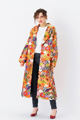 A woman is wearing an oversized silk coat for women. This long silk coat embodies the essence of a long coat for women. Its surface is adorned with intricate silk embroidery, exemplifying the artistry behind a silk embroidered coat for women. The coat's length accentuates its elegance, making it a perfect representation of a long embroidered coat. The oversized nature of this oversized coat for women adds a touch of grandeur to the ensemble, combining style and comfort seamlessly.