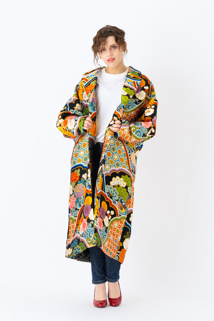 A woman is wearing an oversized silk coat for women. This long silk coat embodies the essence of a long coat for women. Its surface is adorned with intricate silk embroidery, exemplifying the artistry behind a silk embroidered coat for women. The coat's length accentuates its elegance, making it a perfect representation of a long embroidered coat. The oversized nature of this oversized coat for women adds a touch of grandeur to the ensemble, combining style and comfort seamlessly.